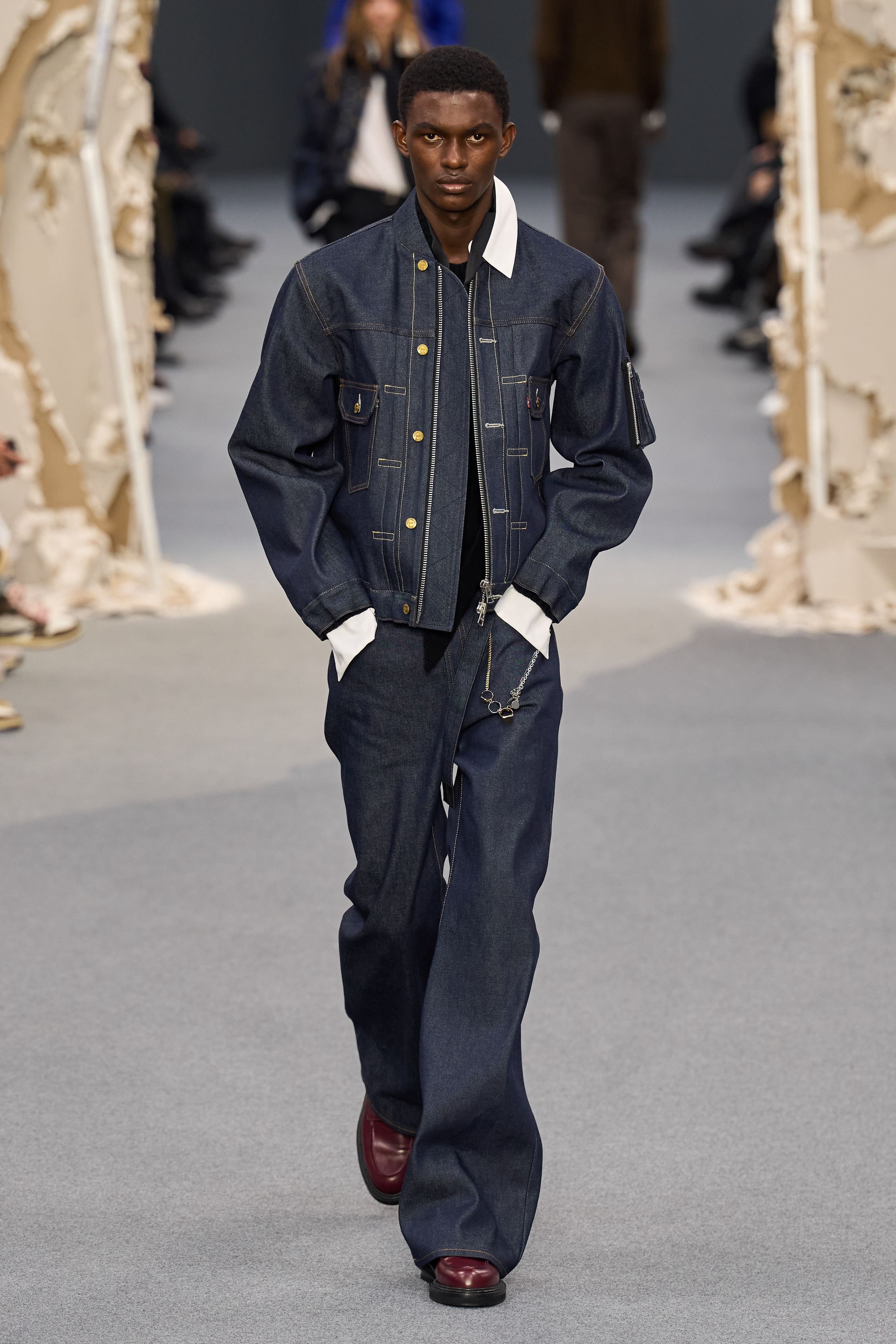Sacai 2026秋冬再次展示其无可复制的“混合美学”。正装、牛仔、皮草与制服元素被高度结构化地拼接，形成既熟悉又陌生的服装形态。性别边界被进一步模糊，层叠结构制造流动节奏，使行走本身成为设计的一部分。系列在秩序与混乱之间找到平衡，是Sacai 对当代复杂生活状态的持续回应-顽石频道趋势研究